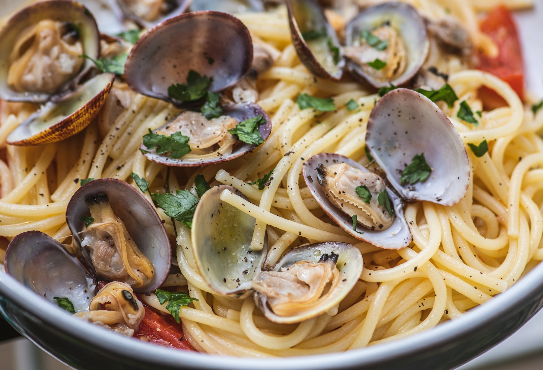 Spaghetti with clams, fresh cherry tomatoes, parsley leaves and ground black pepper