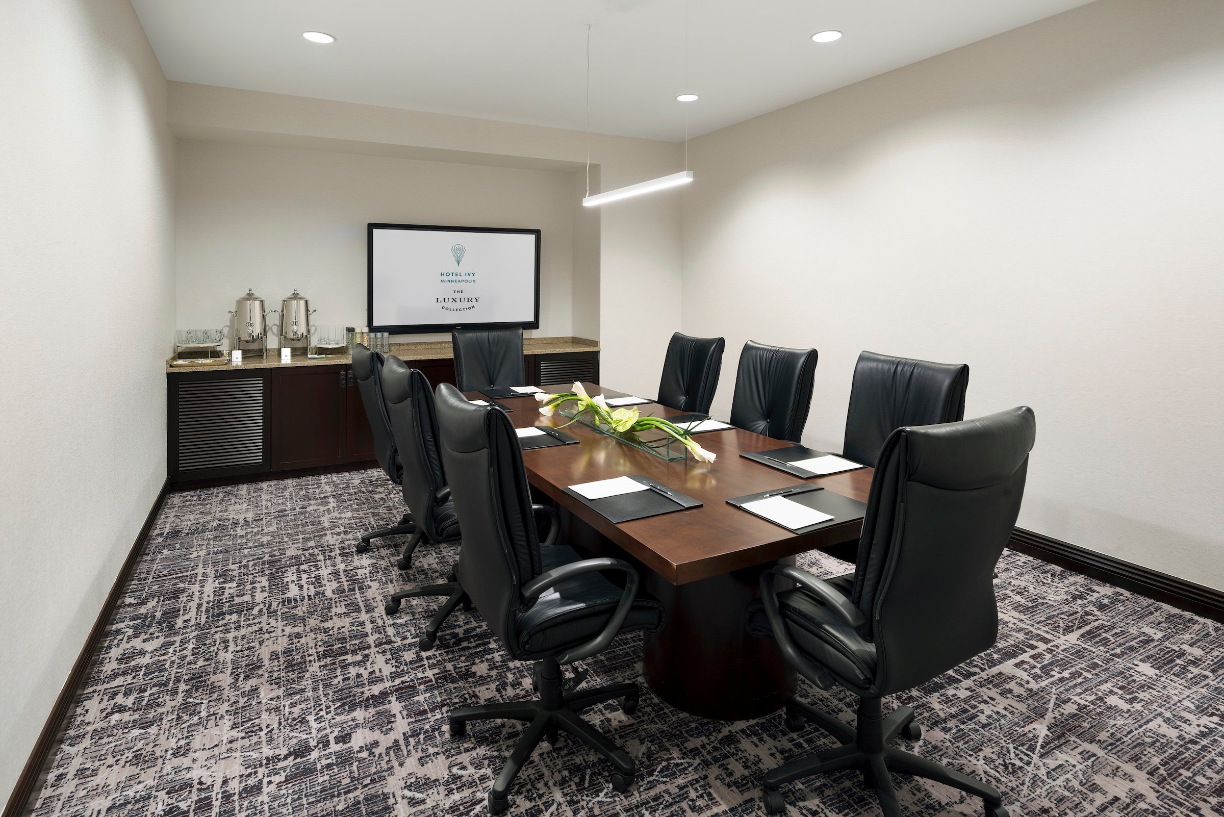 A wooden desk and black leather office chairs with the screen and amenities set up in a meeting venue, Boardroom at Hotel Ivy