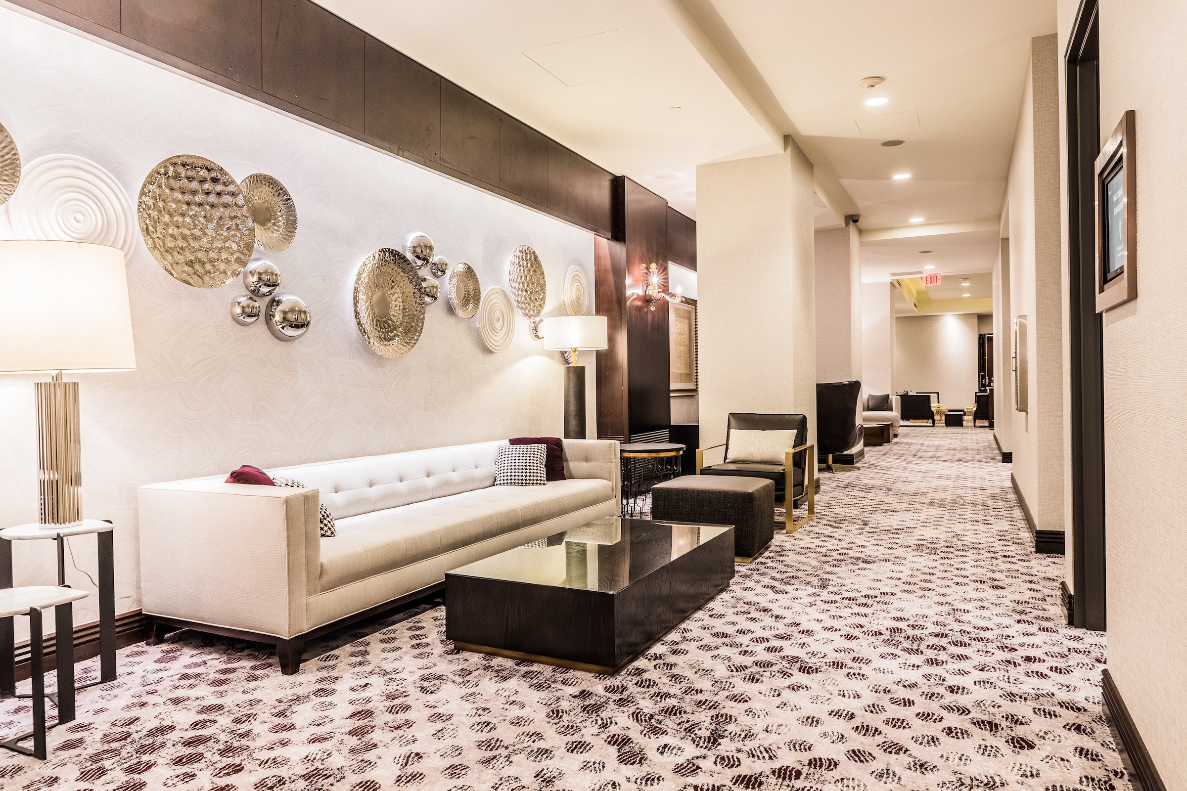 Circular decorations with various materials on a wall with a white couch, dark marble tea table, etc. in a white classic modern space from the hallway of Pre-function space at Hotel Ivy