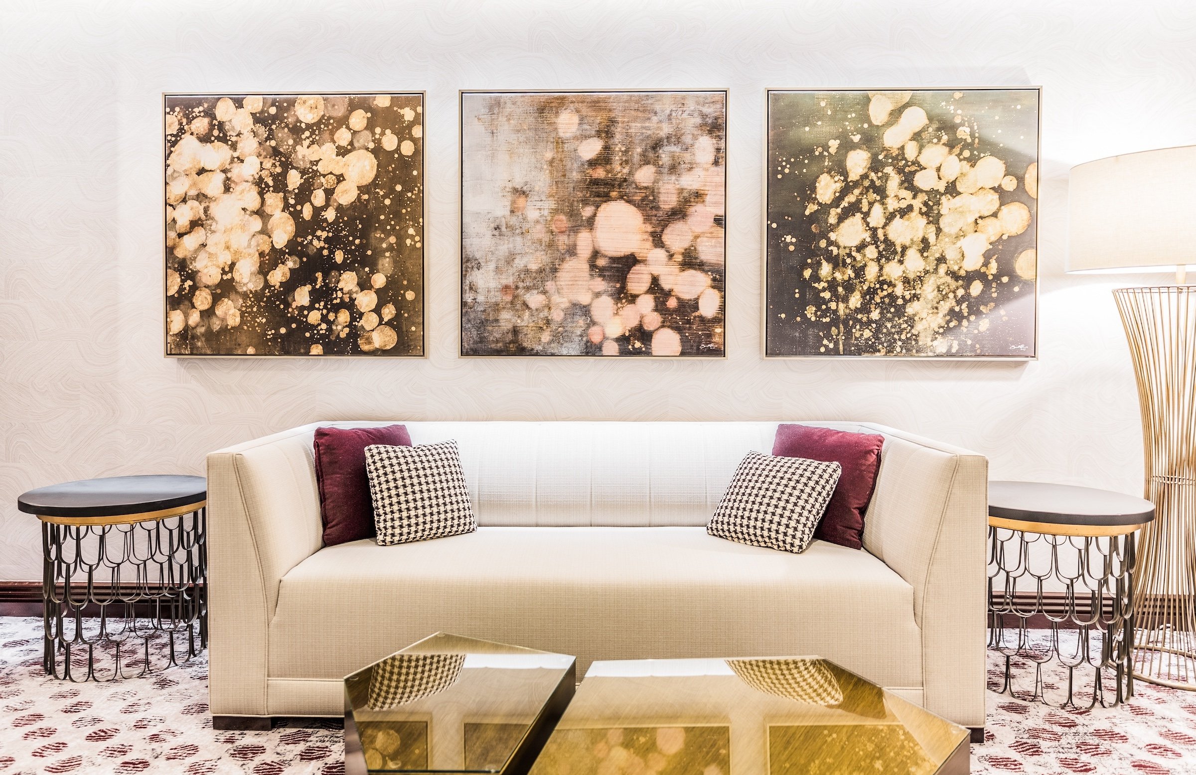 Three paintings with various materials on a wall with a white couch, dark marble tea table, etc. in a white classic modern space, Pre-function space at Hotel Ivy