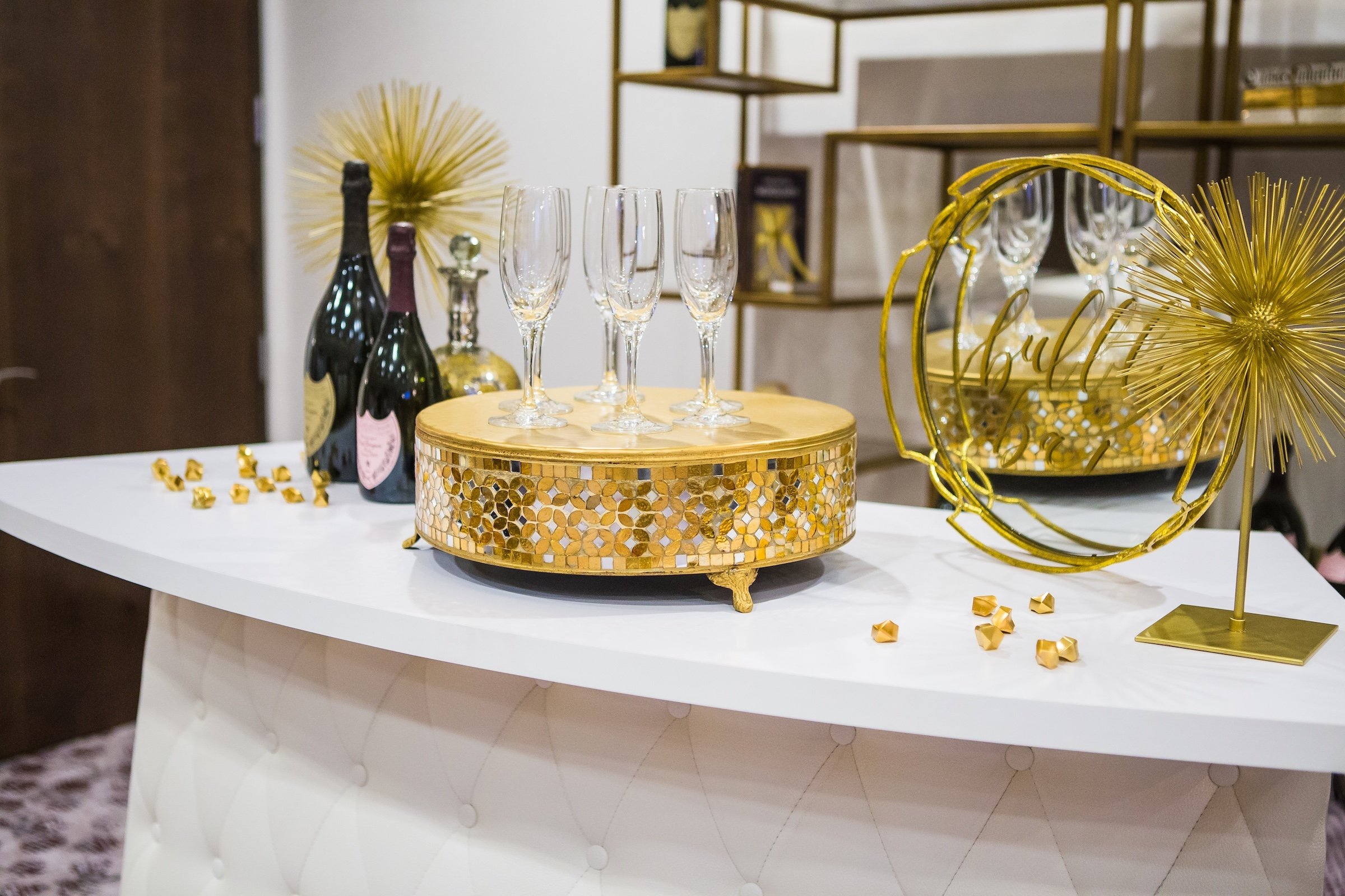 Event details of champagne bottles and glasses with golden decorations on a white reception table at Pre-function Space from Hotel Ivy