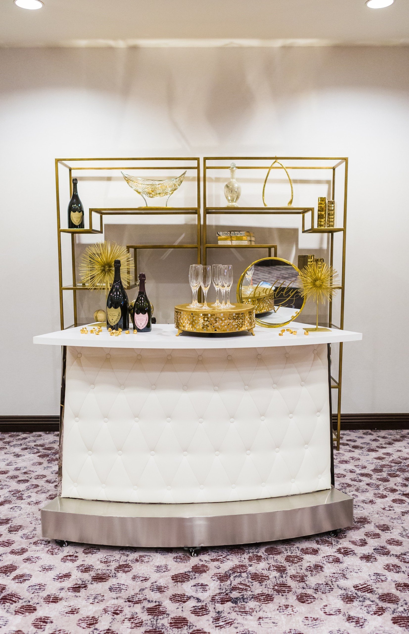 Liquor tables with golden decorations on a white reception table in Pre-function Space at Hotel Ivy