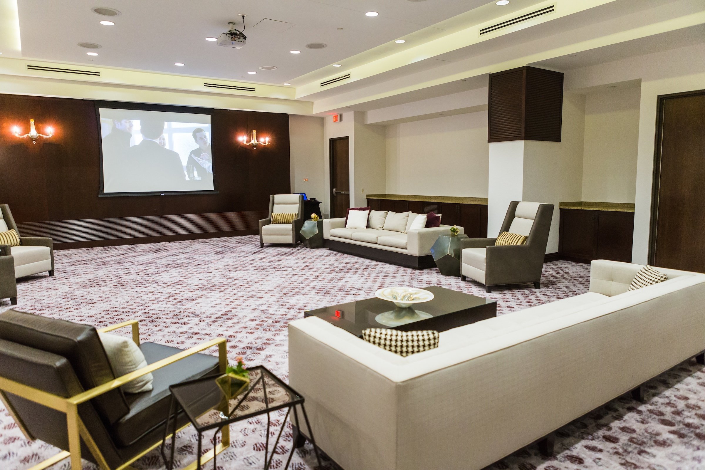 A screen playing video with few comfortable couches around in a large event venue, Pre-function Space at Hotel Ivy