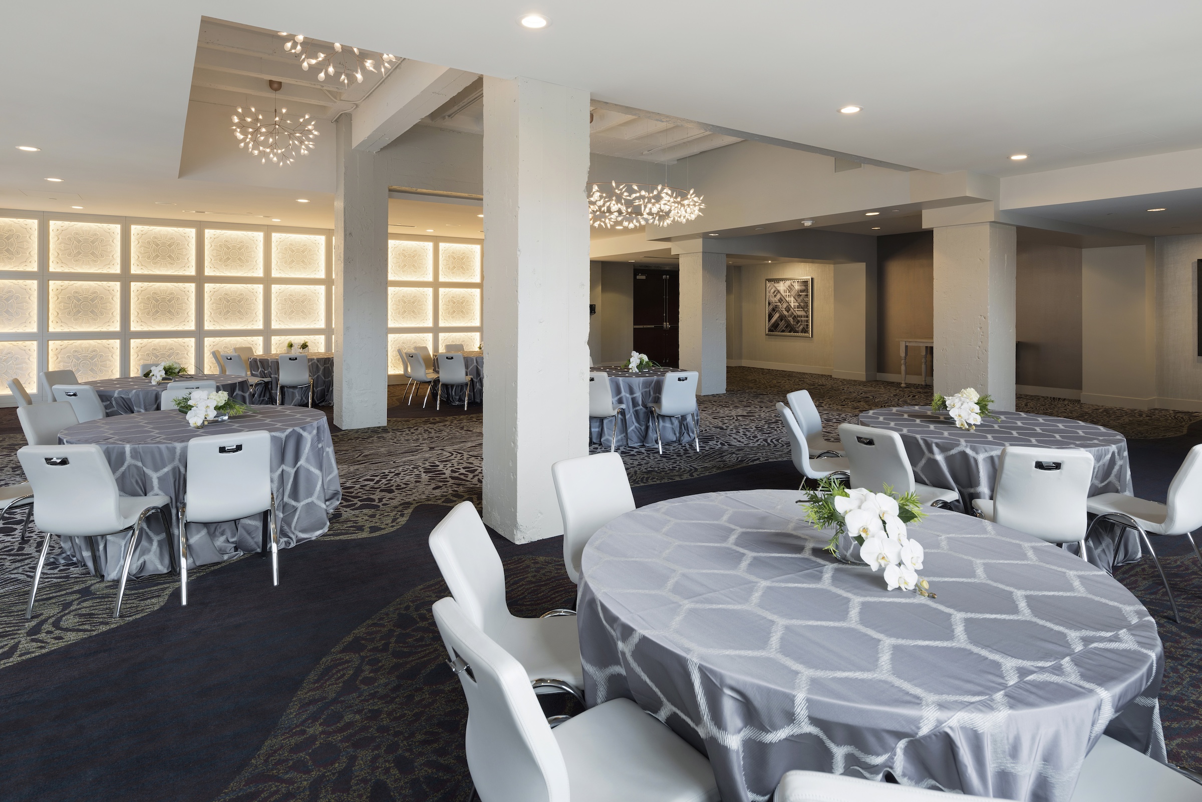 Several round tables with grey cloth and chairs under unique lights in a large event space, Grand Studio at Hotel Ivy