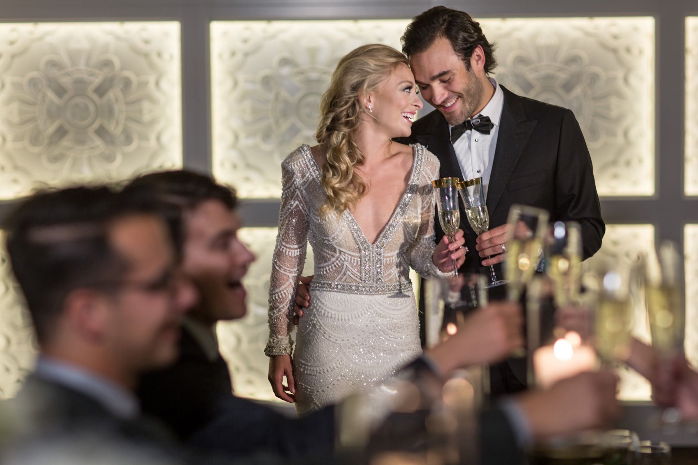 A bride with gorgeous dress and a groom with black suit are cheering champagne in front of the crowd for their wedding at Hotel Ivy