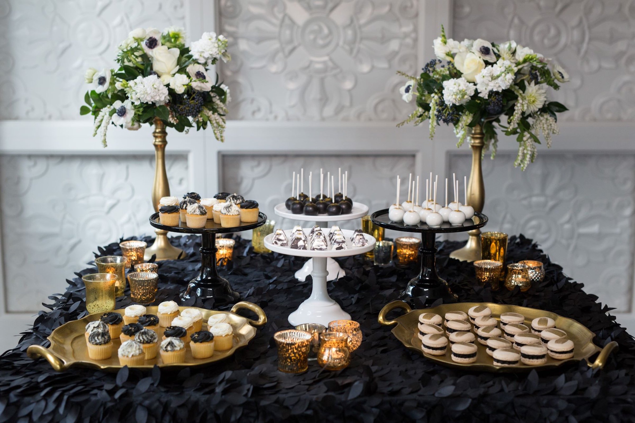 gourmet desserts - cream cupcakes, coffee macarons, dark and white chocolates - with flower bouquets on square table with black cloth for wedding event settings at Hotel Ivy