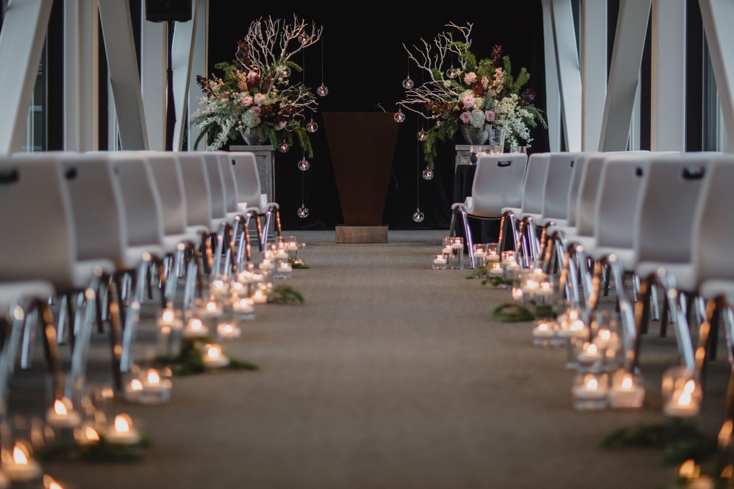 A stylish event set up, several grey chairs for crowd with candles and wooden for weddings in Skyway venue at Hotel Ivy