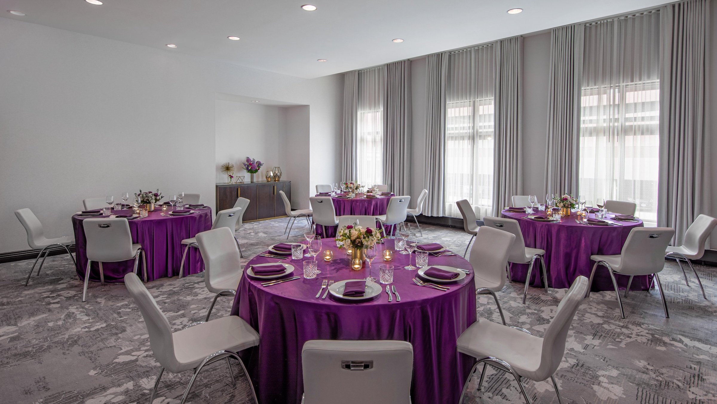 Round tables with purple cloth and grey chairs for dining in an event venue at Hotel Ivy