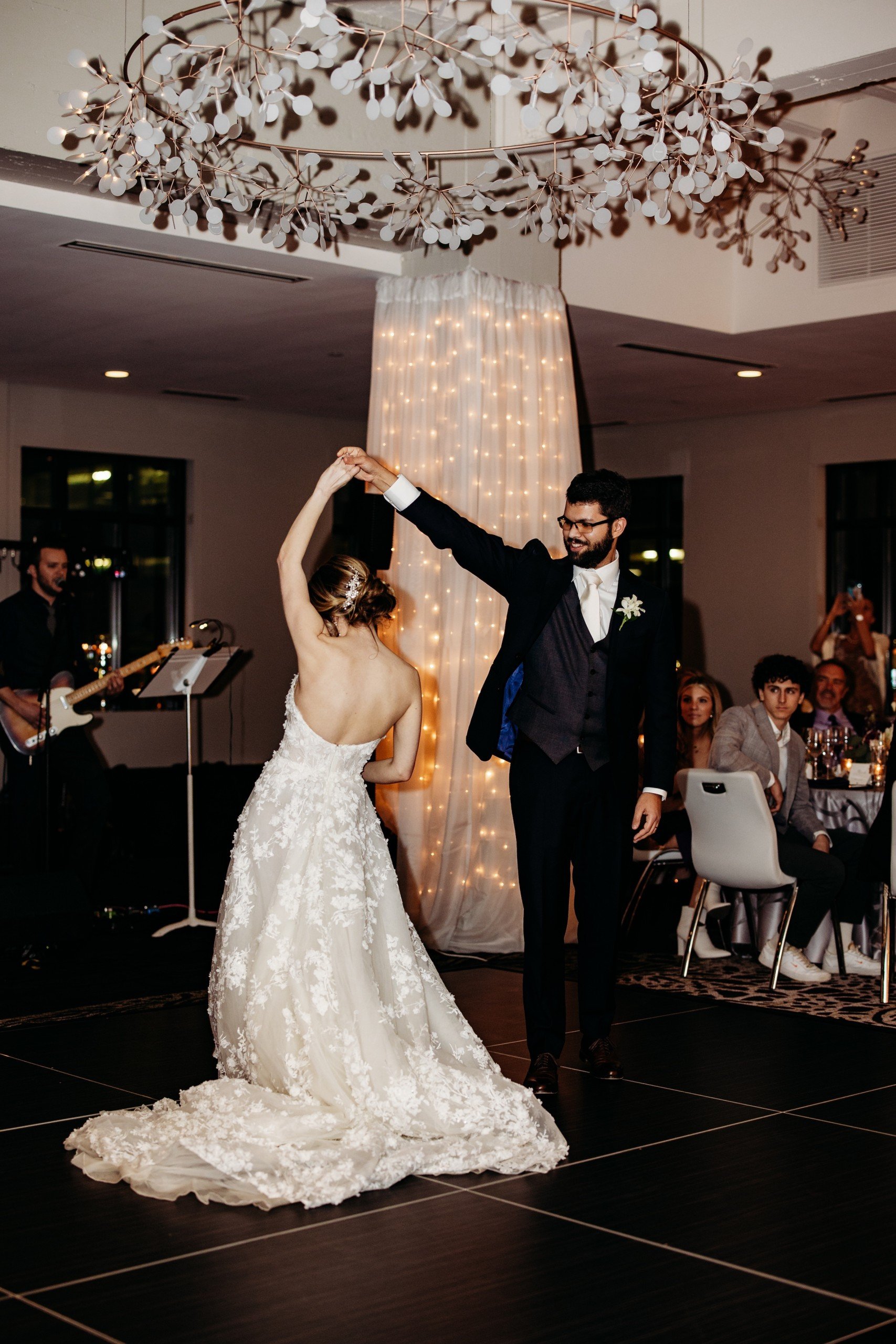 Main hosts of the wedding, Granby and Sprung, are dancing in front of the crowd with people playing instruments under sophisticated light decorations at Grand Studio of Hotel Ivy