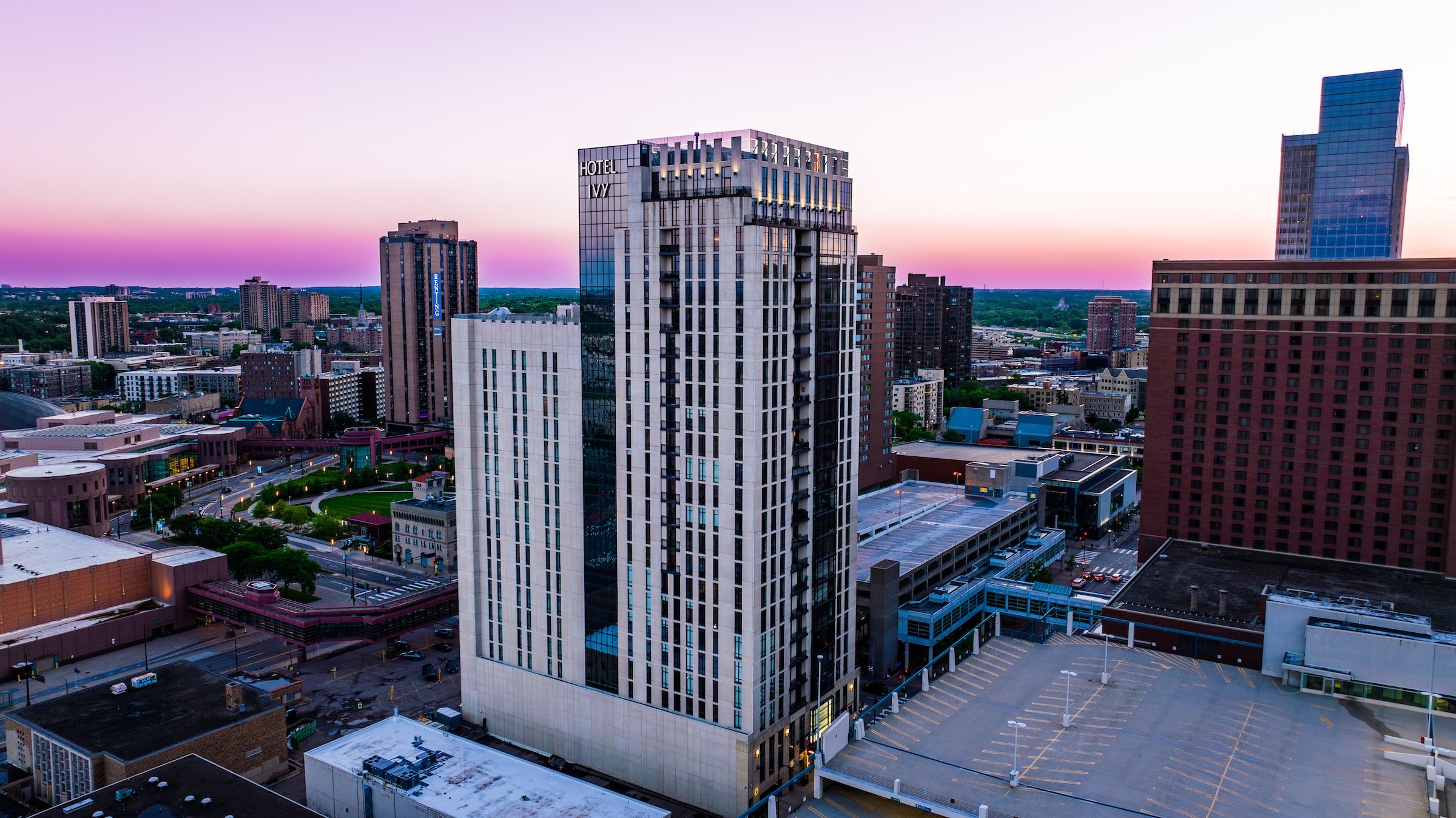 A white tall building with glass of Hotel Ivy with city view under pink sky