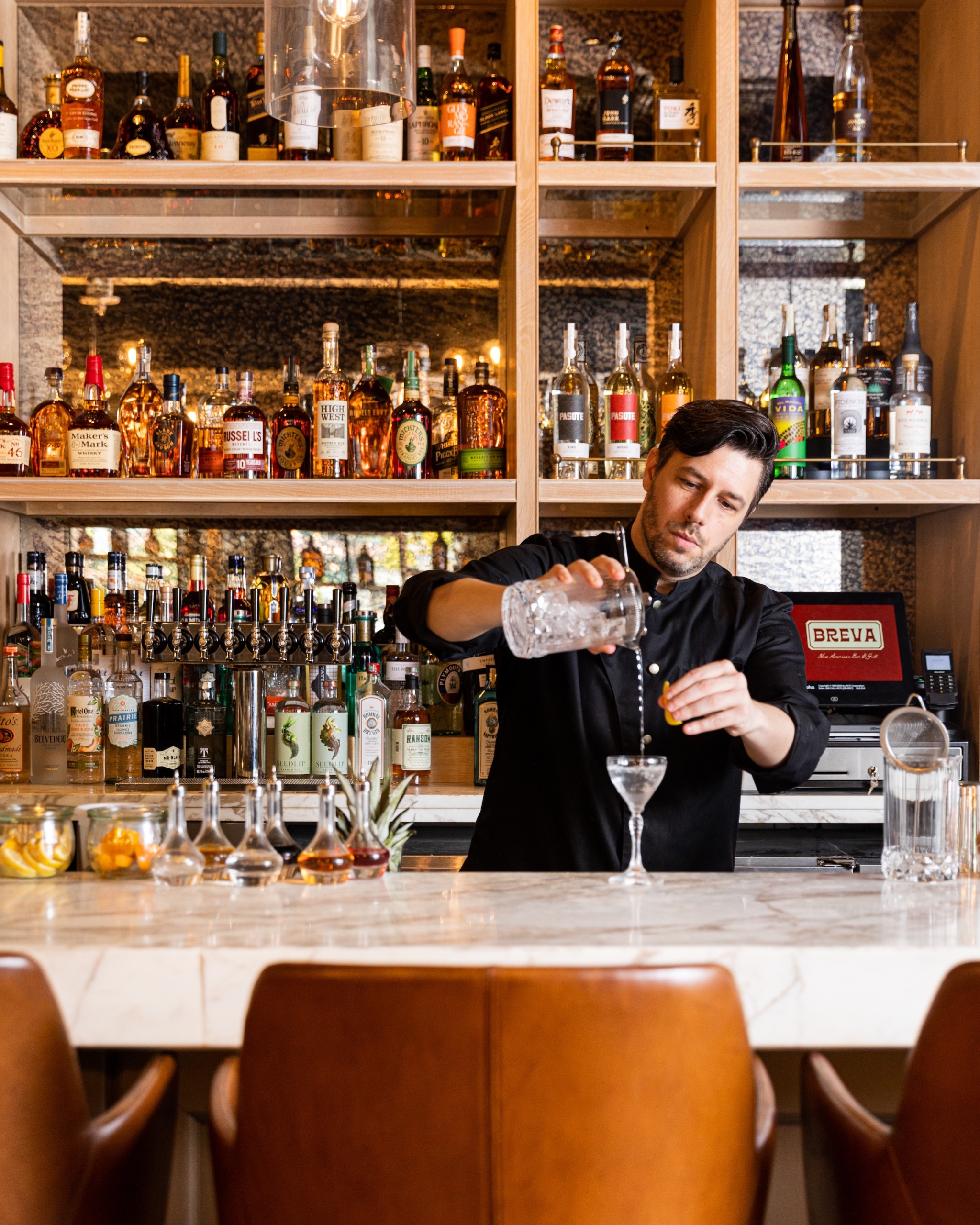 A bartender making a cocktails on white marble bar table with leather chairs at Breva