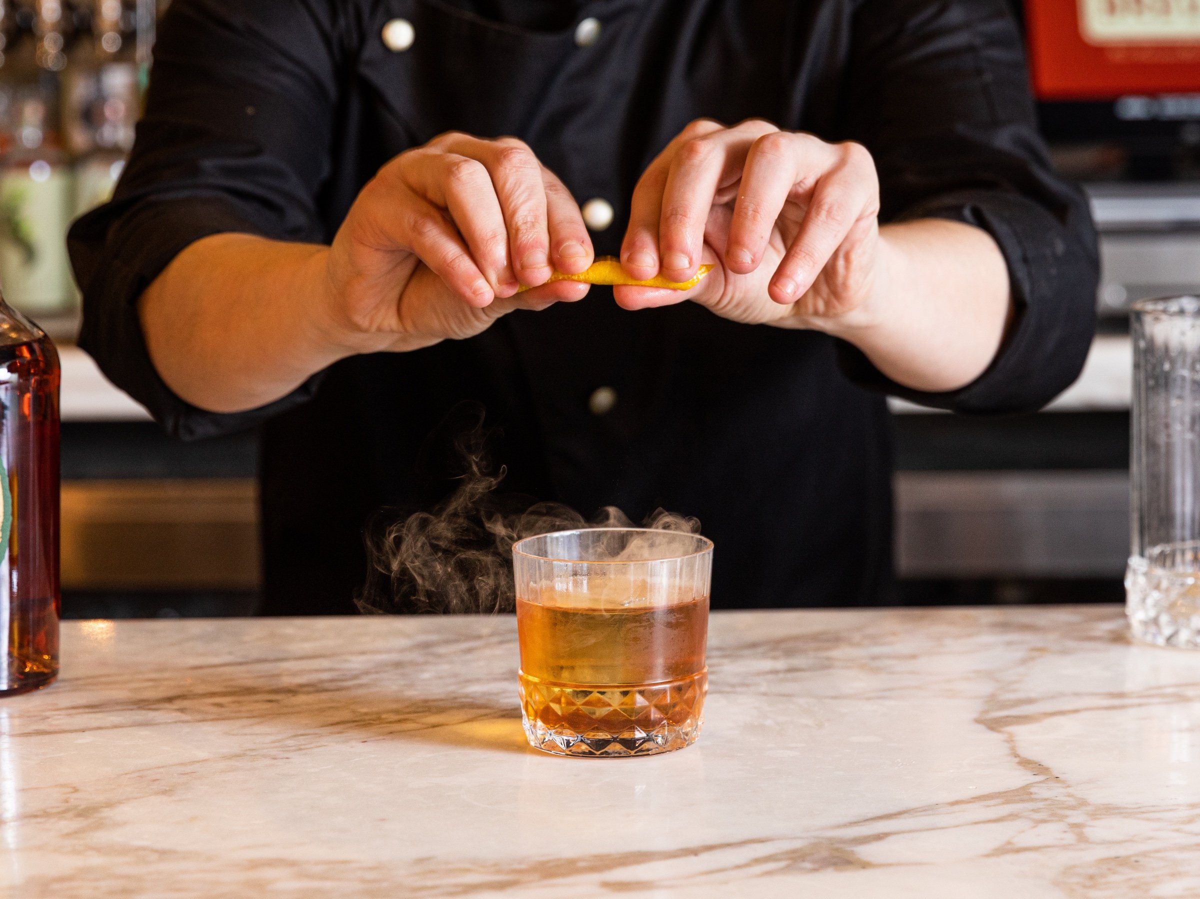 A bartender squeezing a lemon to fig old fashioned cocktail at Breva