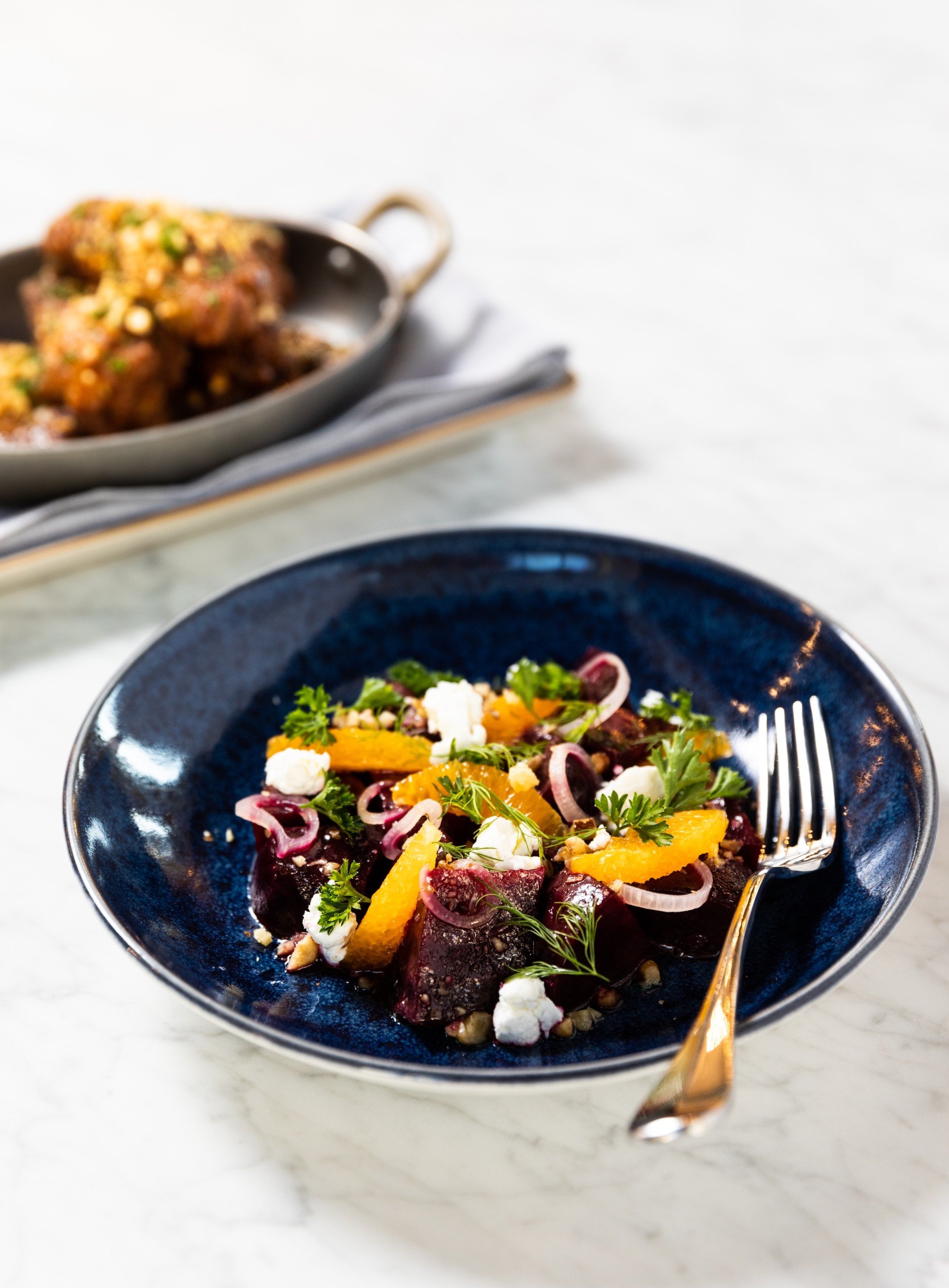 Roasted beet salad in a navy ceramic bowl with other cuisine on a white marble table at Breva from Hotel Ivy