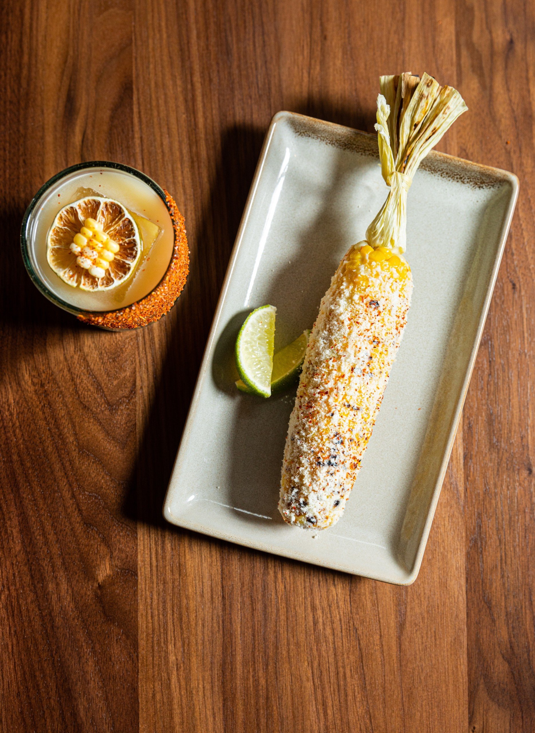 Elotes with limes on an ivory dish and cocktails with dried fruit on a wooden table at Masa & Agave from Hotel Ivy