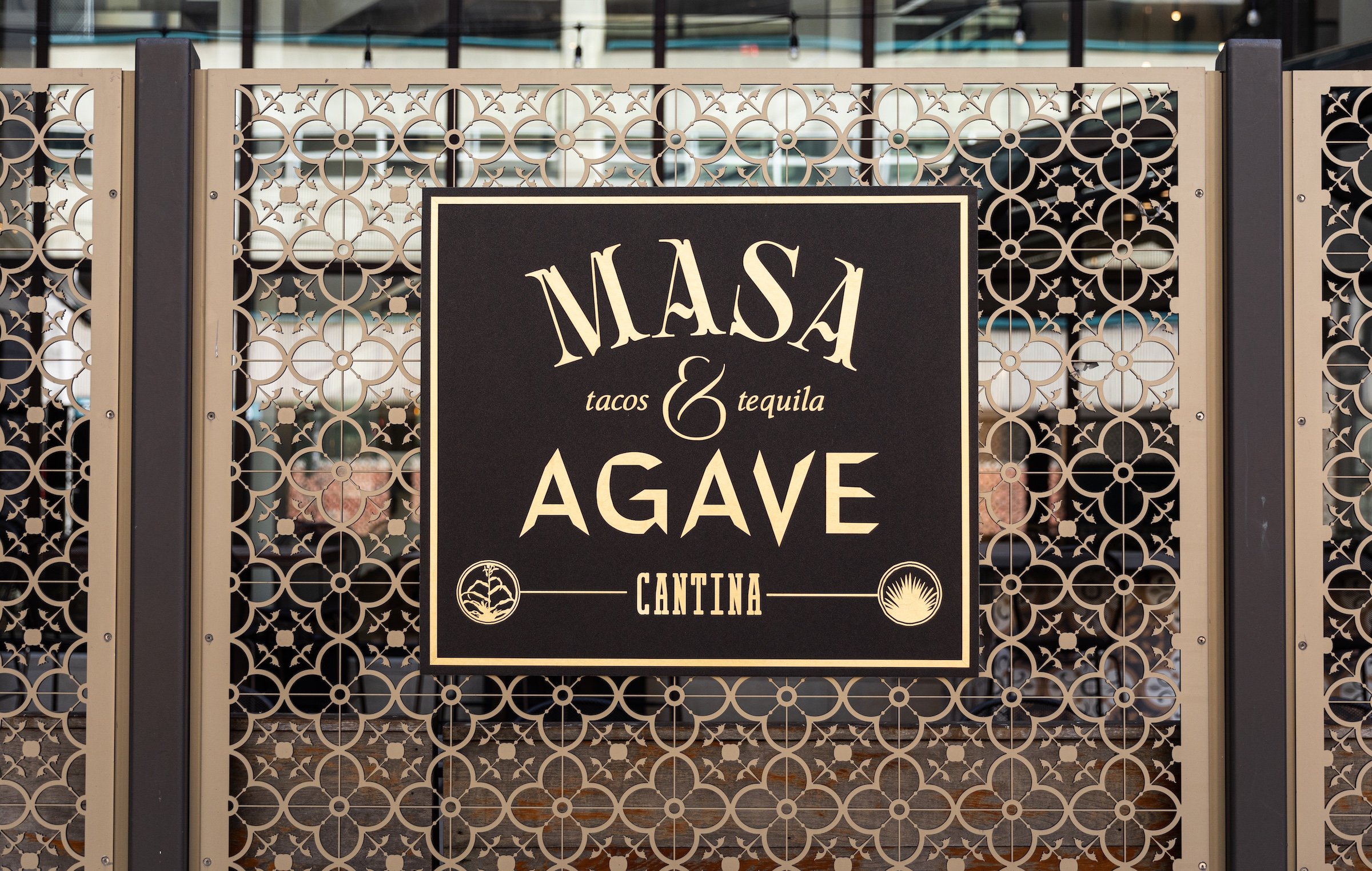 Dark wooden signboard with golden lettering of Masa & Agave, concentrating Catina experience of tacos and tequila from unique patterned outdoor entrance