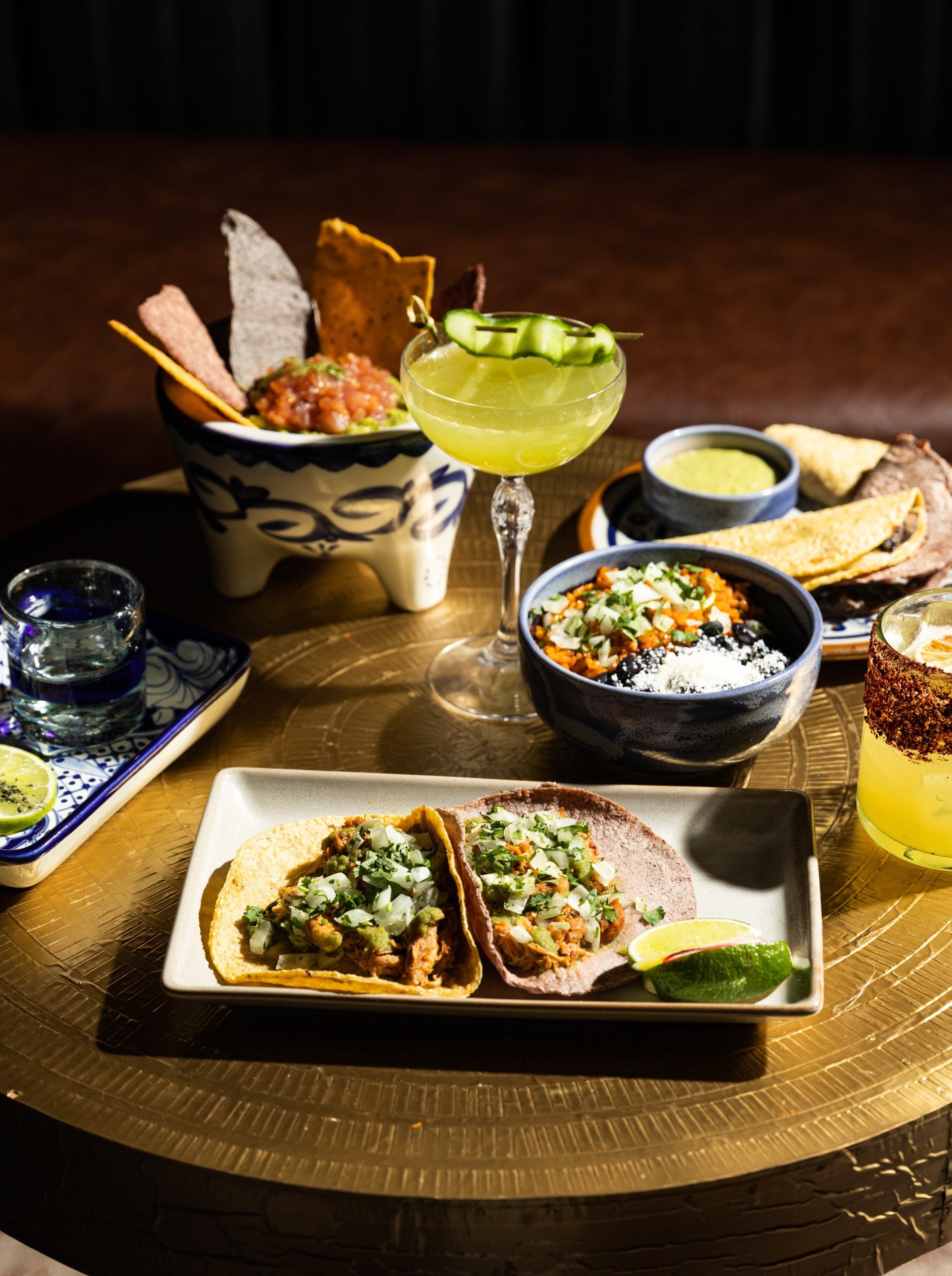 Colourful dishes of tacos, mexican bowl, nachos, cocktails on a golden table at Masa & Agave from Hotel Ivy