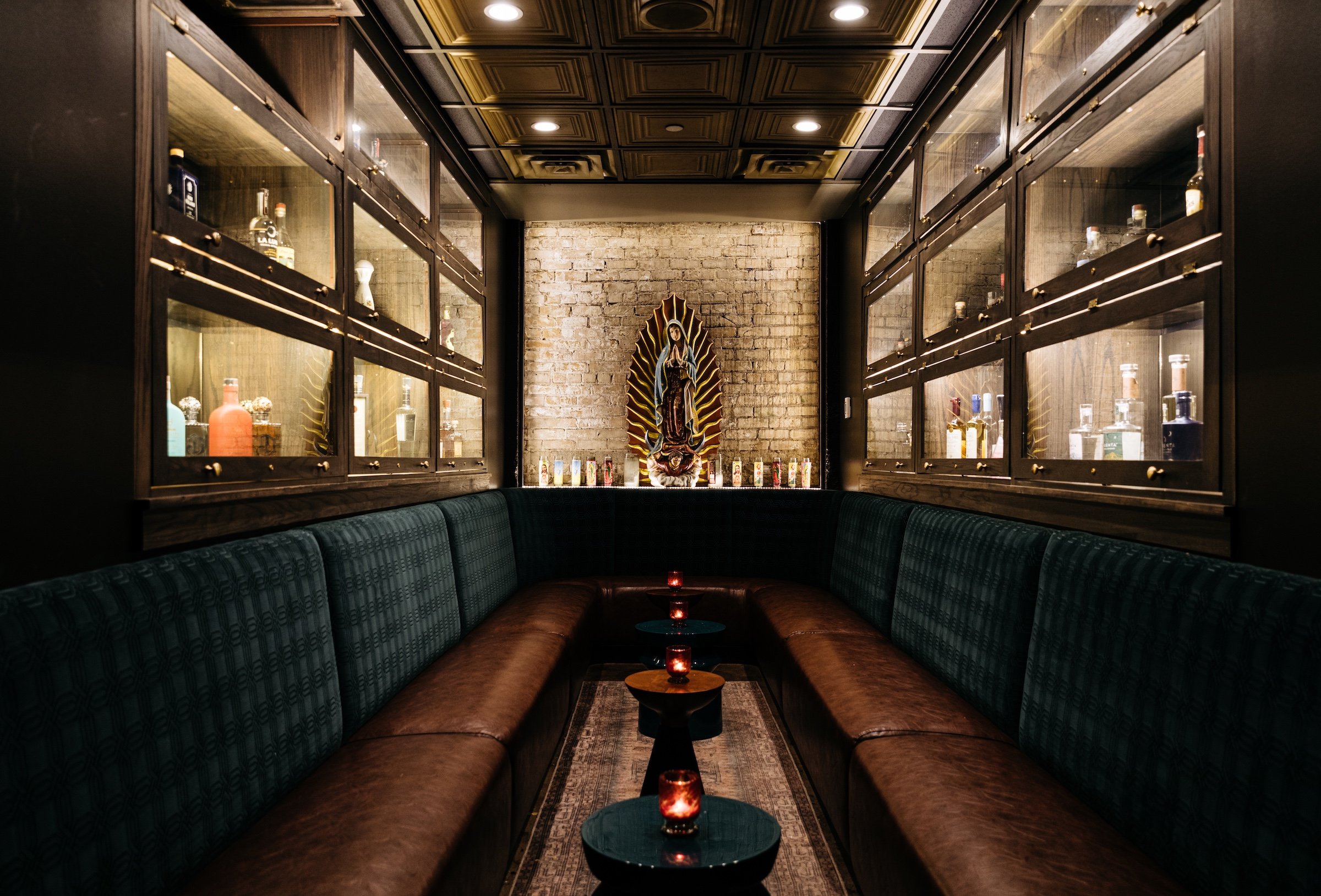 A sacred woman status, U-shaped comfortable couch with small round tables next to Tequila collections in Tequila Chapel from Masa & Agave of Hotel Ivy