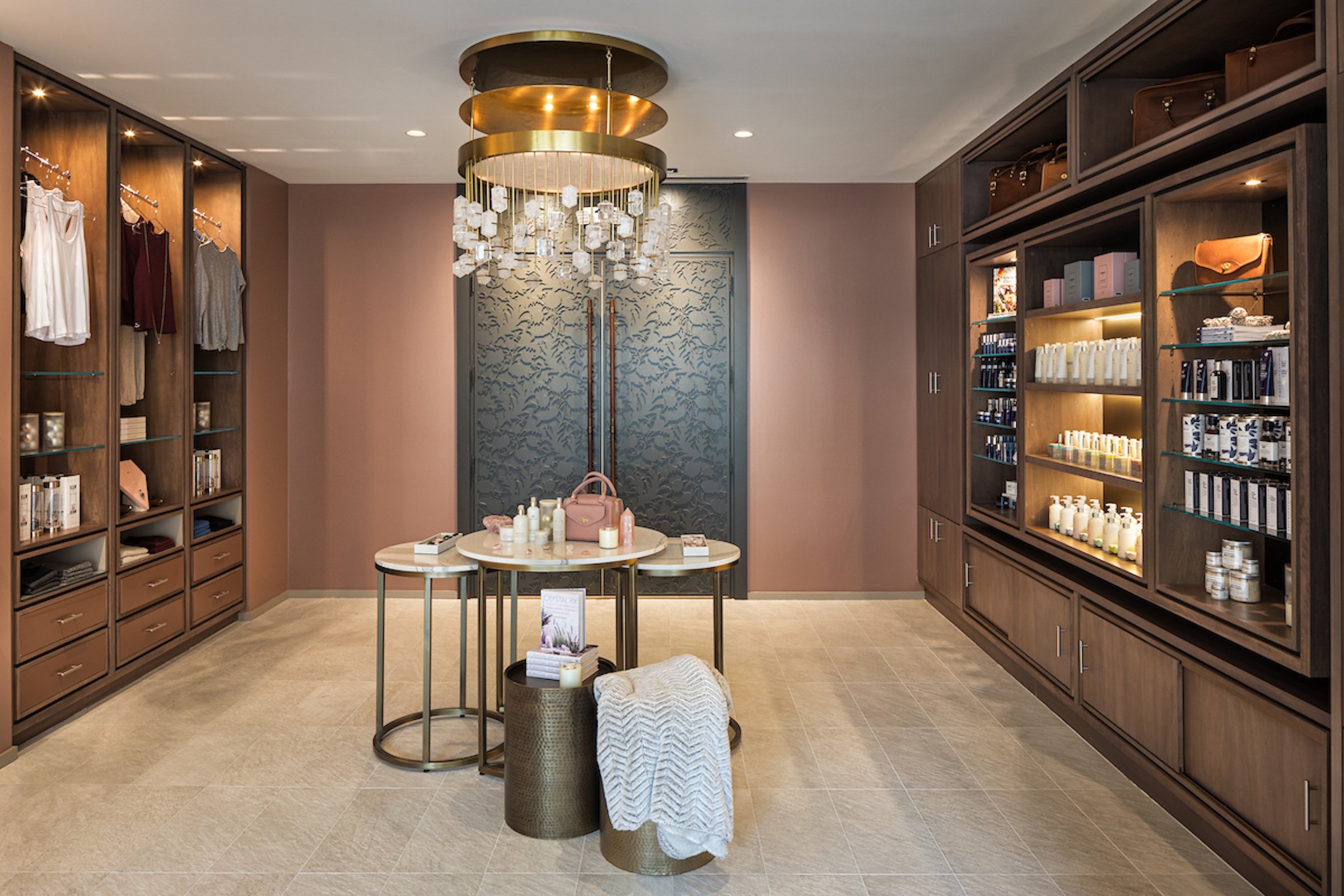 Amenities displayed on white marble tables and large shelves for retails under unique chandelier at Anda Spa of Hotel Ivy