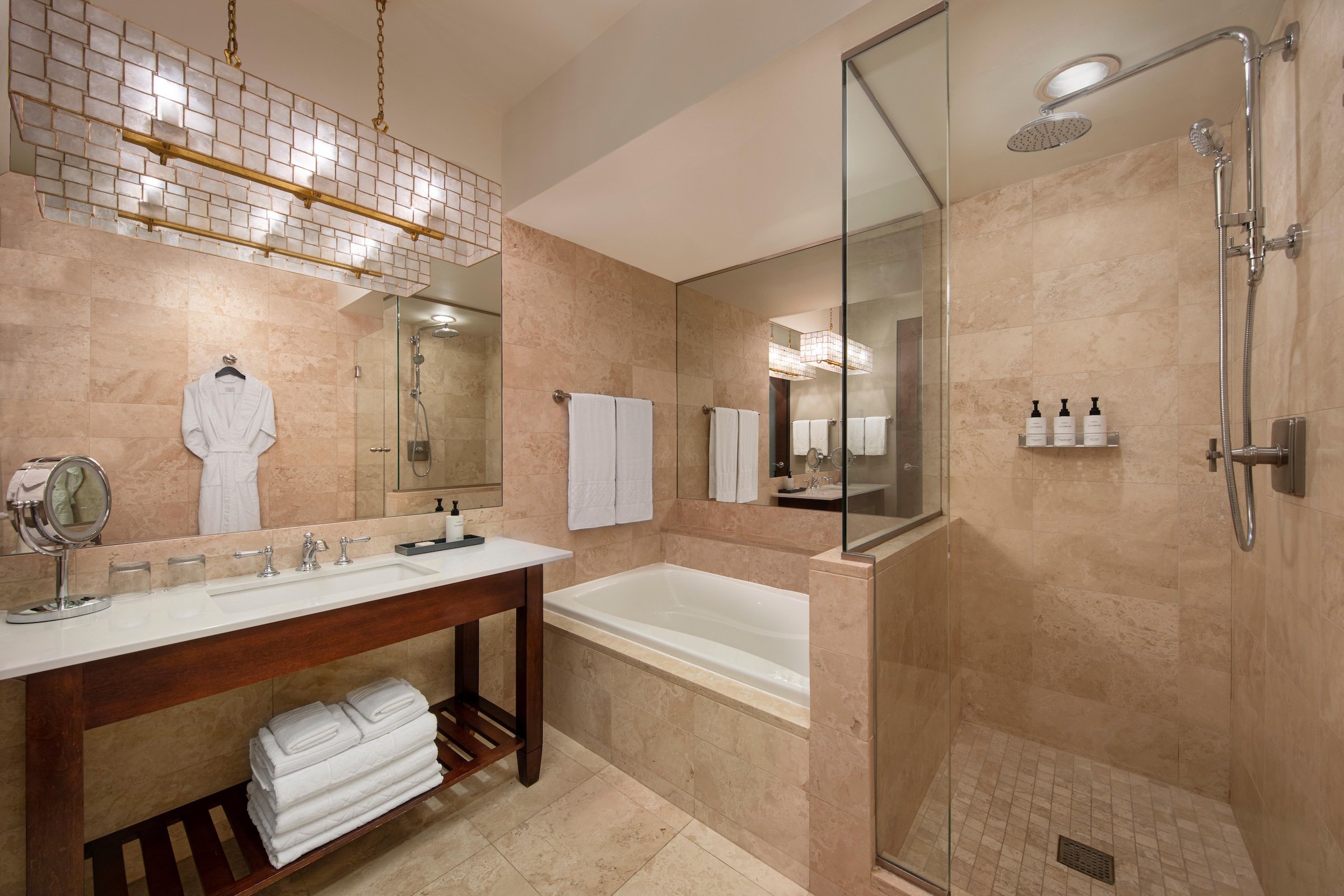 A rainfall shower booth, a white bathtub and a sink in a bathroom with brown marble wall at Hotel Ivy