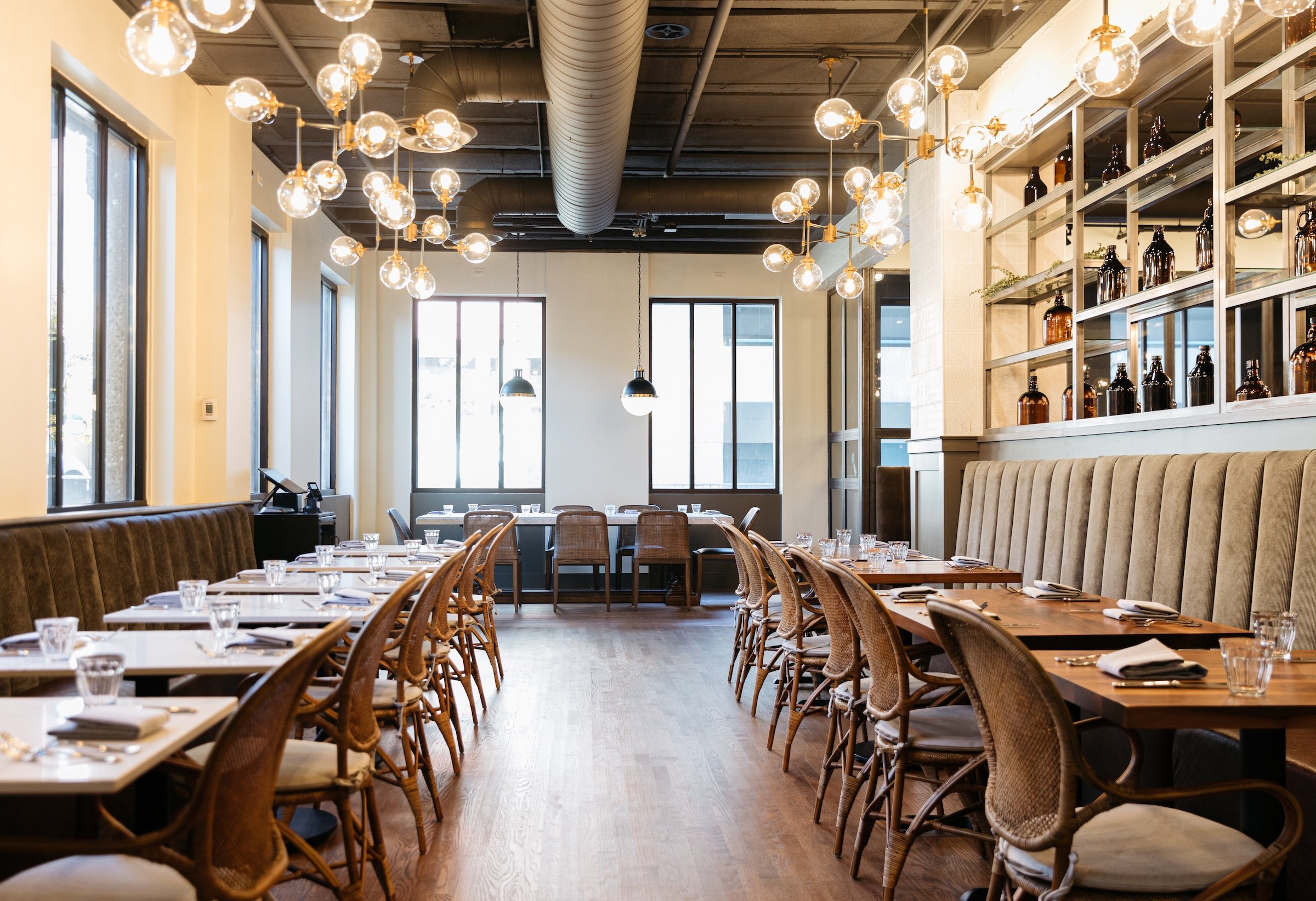 Interior of Breva Bar is & Grill from Hotel Ivy - Dining tables with large glass under round light bulbs in a bright space