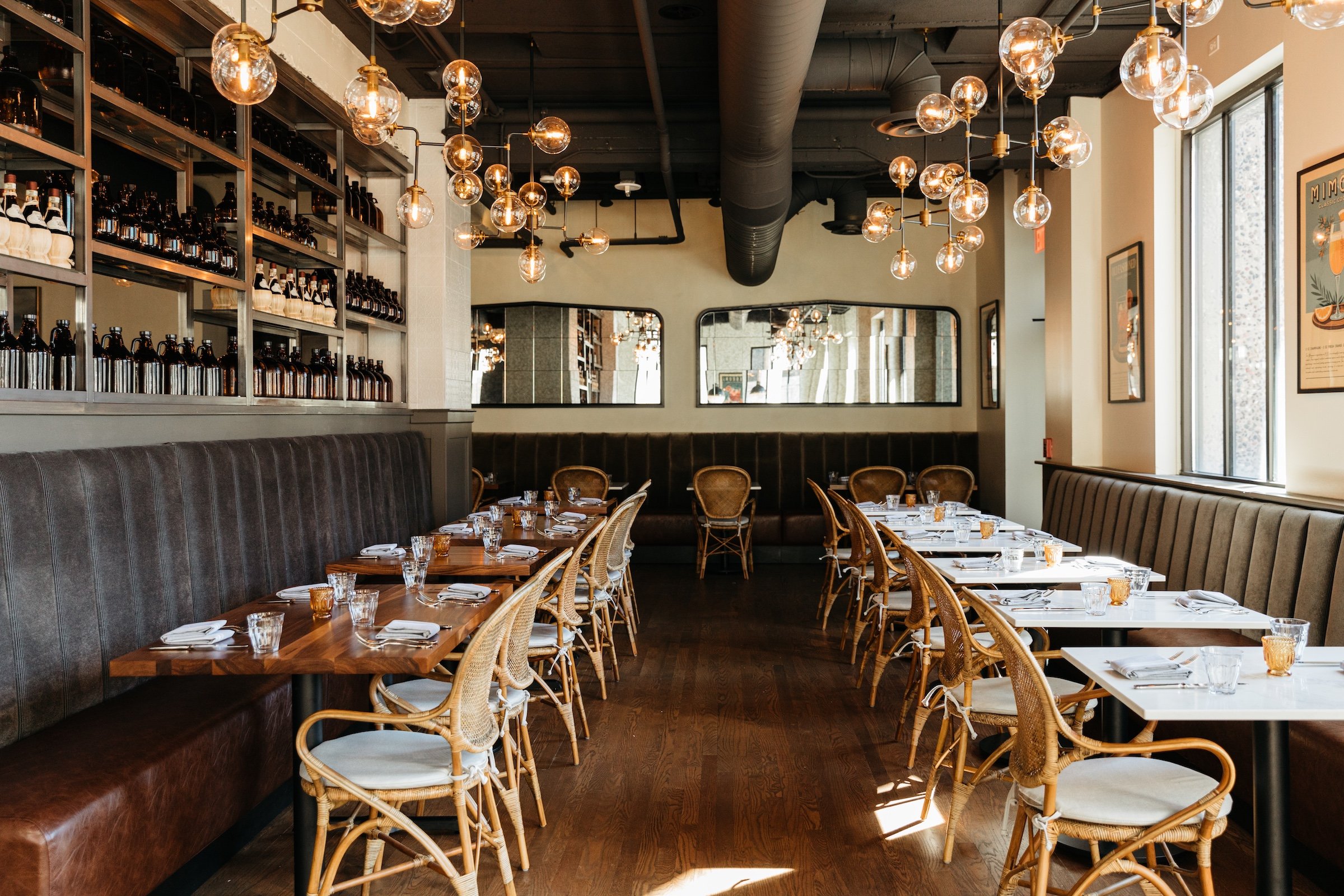 Interior of Breva Bar is & Grill from Hotel Ivy - Dining tables with large glass and mirrors under round light bulbs and a pipe in a bright space