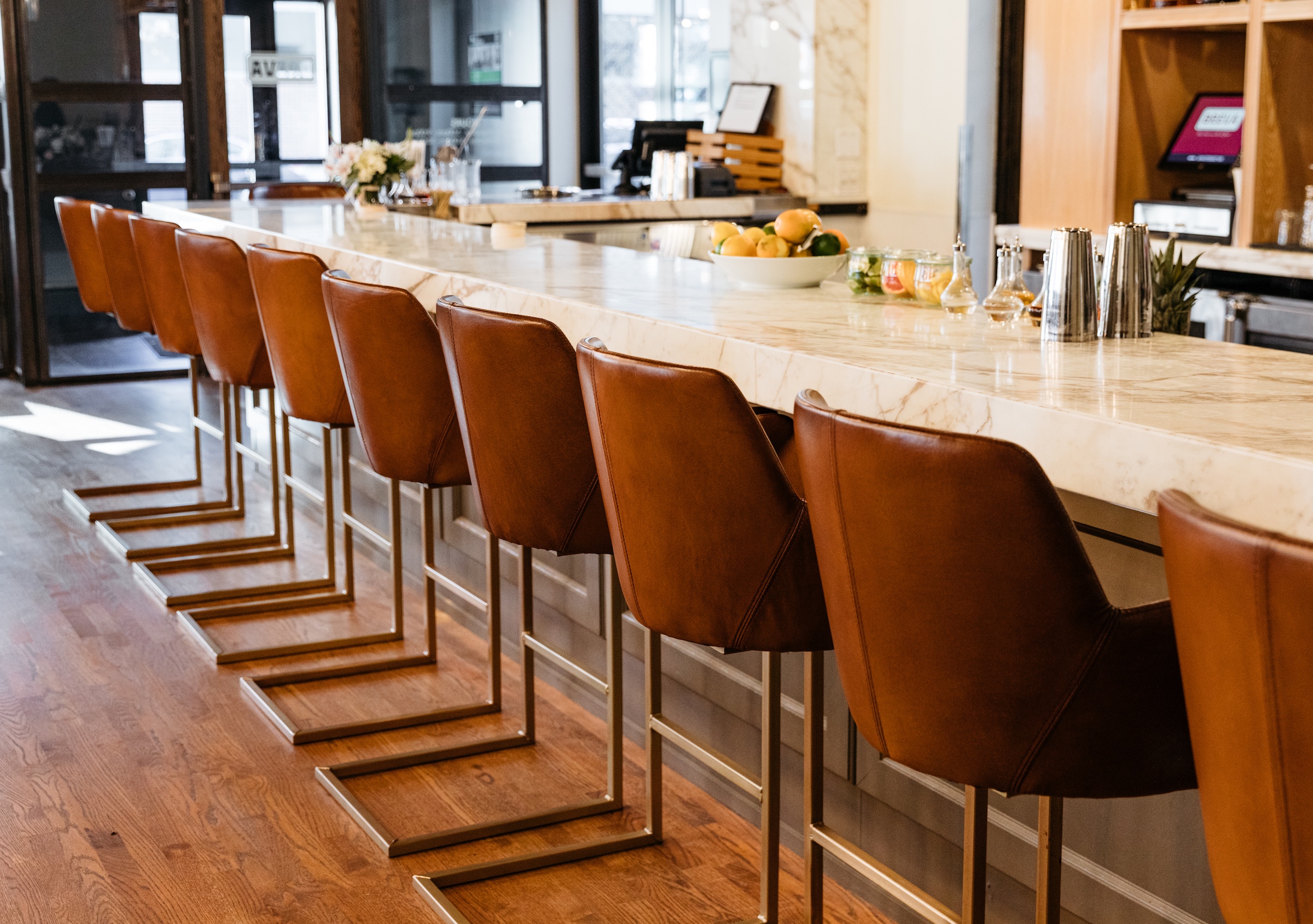 Fruits, some spice on a marble white bar table and brown leather high chairs next to P.O.S in a bright space, Breva Bar & Grill from Hotel Ivy